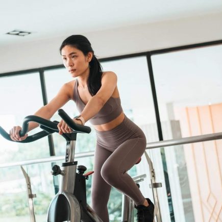 femme qui fait 30 minutes de vélo d'appartement par jour chez elle pour maigrir ou renforcer ses muscles